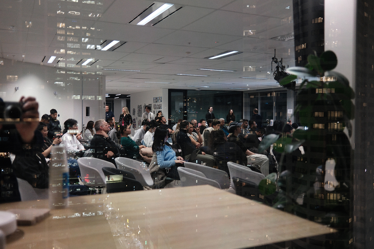 The Meetup 03 audience is seen through reflections of Sydney office lights at night.